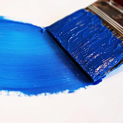 Close-up of a vivid blue brushstroke applied to a white canvas using a paintbrush.
